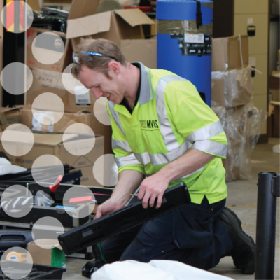 Tom Hooton in a yellow high visual jacket and a screwdriver in front of some dots separating the background