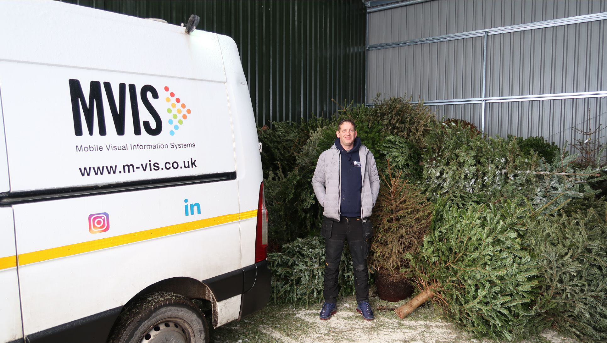 man in a silver coat and navy jumper, standing next to a van in front of a Christmas tree. He is ashgate volunteering