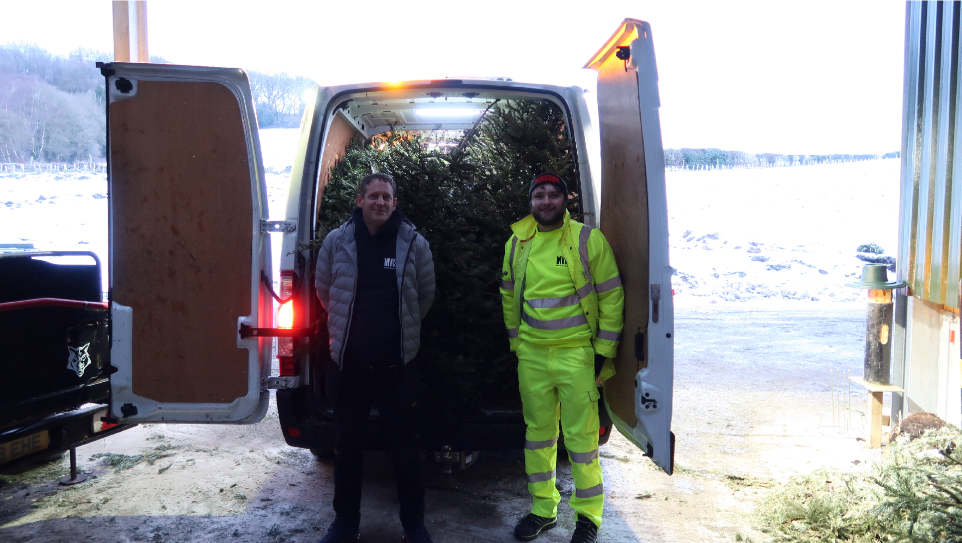 two men in front of a van filled with christmas trees, one wearing high vis and the other wearing a silver coats and navy jacket, they are ashgate volunteering