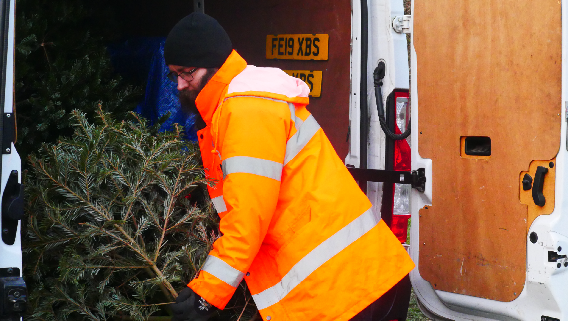 Man in high vis loading a christmas tree into a white van for Treecycle